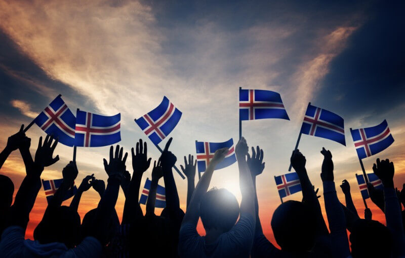 Silhouetted crowd waving Icelandic flags at sunset, celebrating national pride and unity with vibrant colors against a glowing sky.