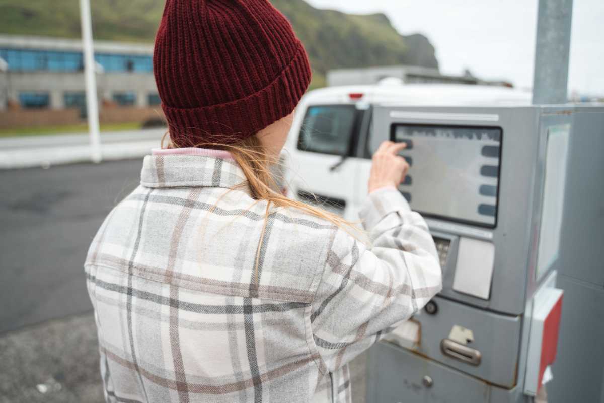 A woman in a cap and plaid shirt manipulates a gas pump in Iceland.