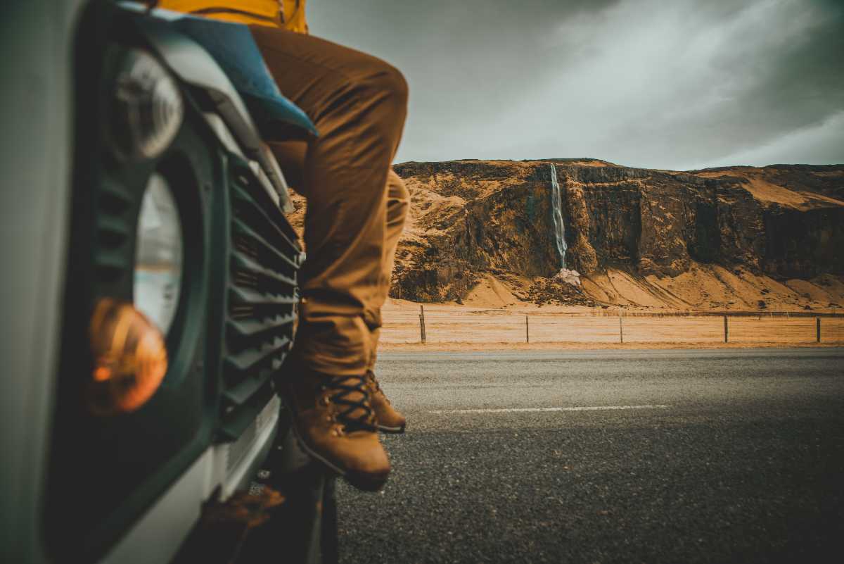 man sitting on top of his rental car by a waterfall in Iceland