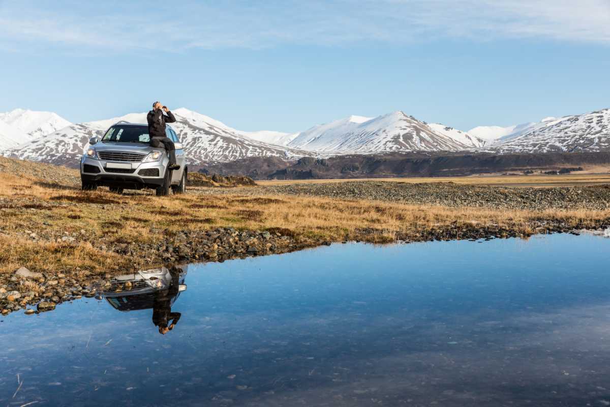 Tourist sitting on top of his rental car by a lake in Iceland