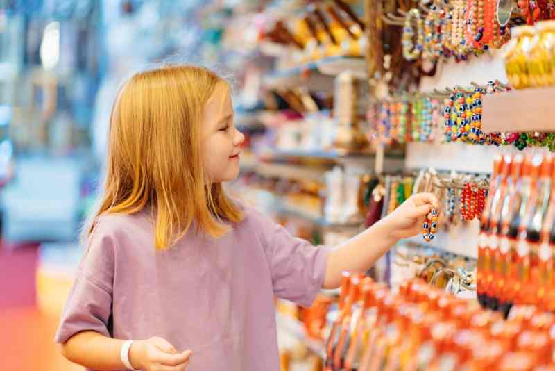 Girl exploring handmade bracelet collection in a vibrant souvenir shop.