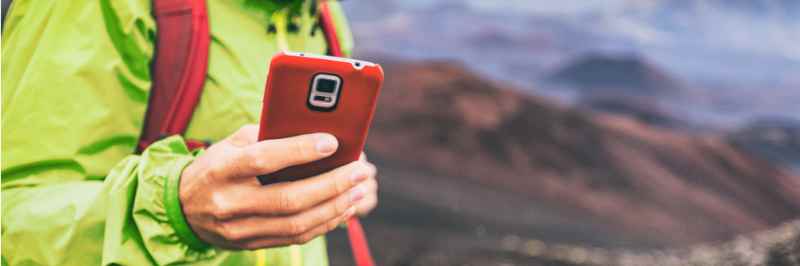 Hiker uses smartphone in Icelandic mountain landscape Hiker in a green jacket holds a red smartphone while exploring Iceland's mountainous terrain.
