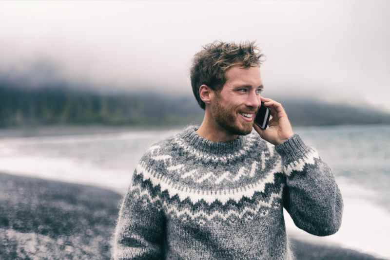 Man in Icelandic sweater talking on the phone on foggy beach Smiling man in a traditional Icelandic wool sweater talking on the phone on a misty beach in Iceland.
