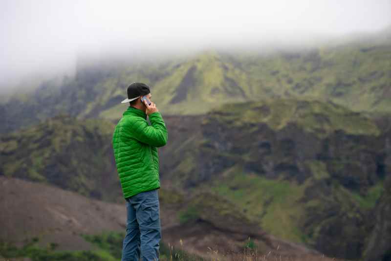 Telephone call in Iceland's misty mountain landscape Man in green jacket talking on the phone in a foggy, mountainous landscape in Iceland.